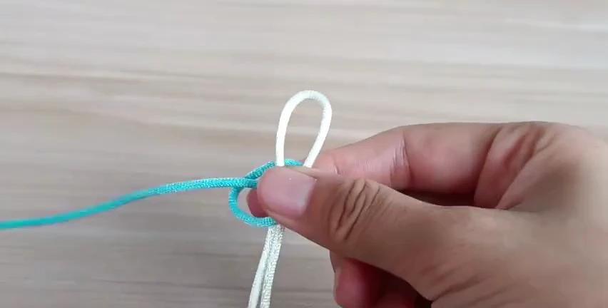 Turquoise working cord returning through a side loop around two white core strands